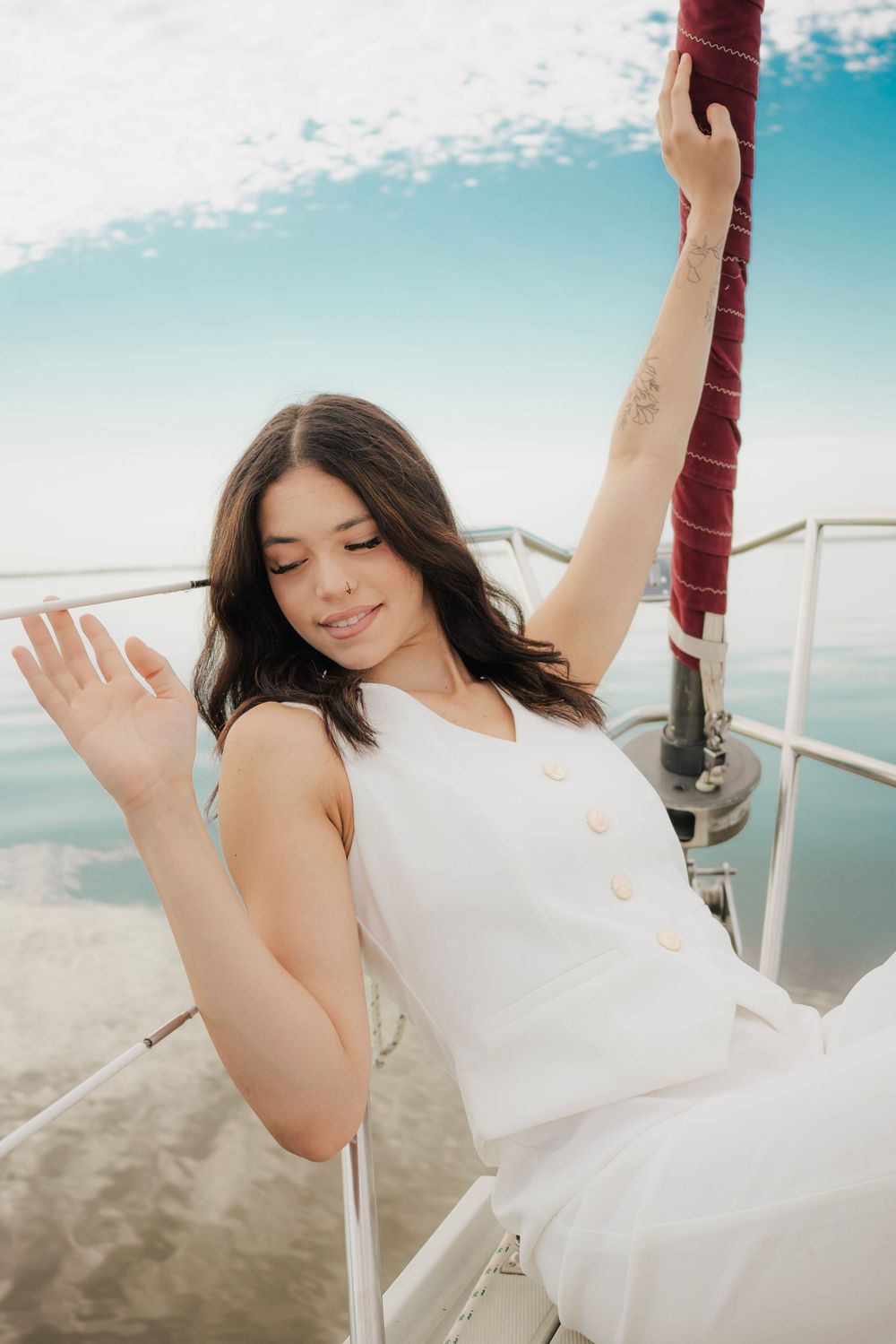 A young woman in white outfit posing on a sailboat deck on a sunny day.