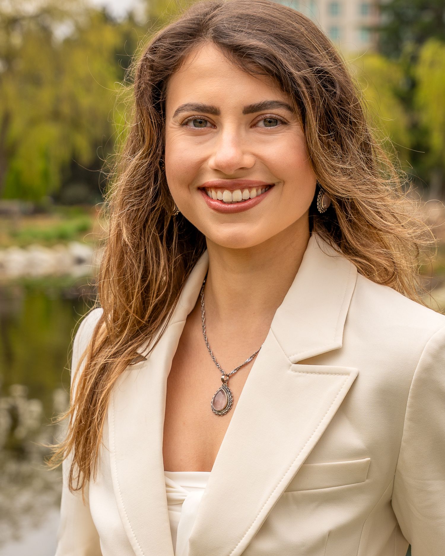 Woman smiling in a cream blazer during an outdoor professional headshot session.