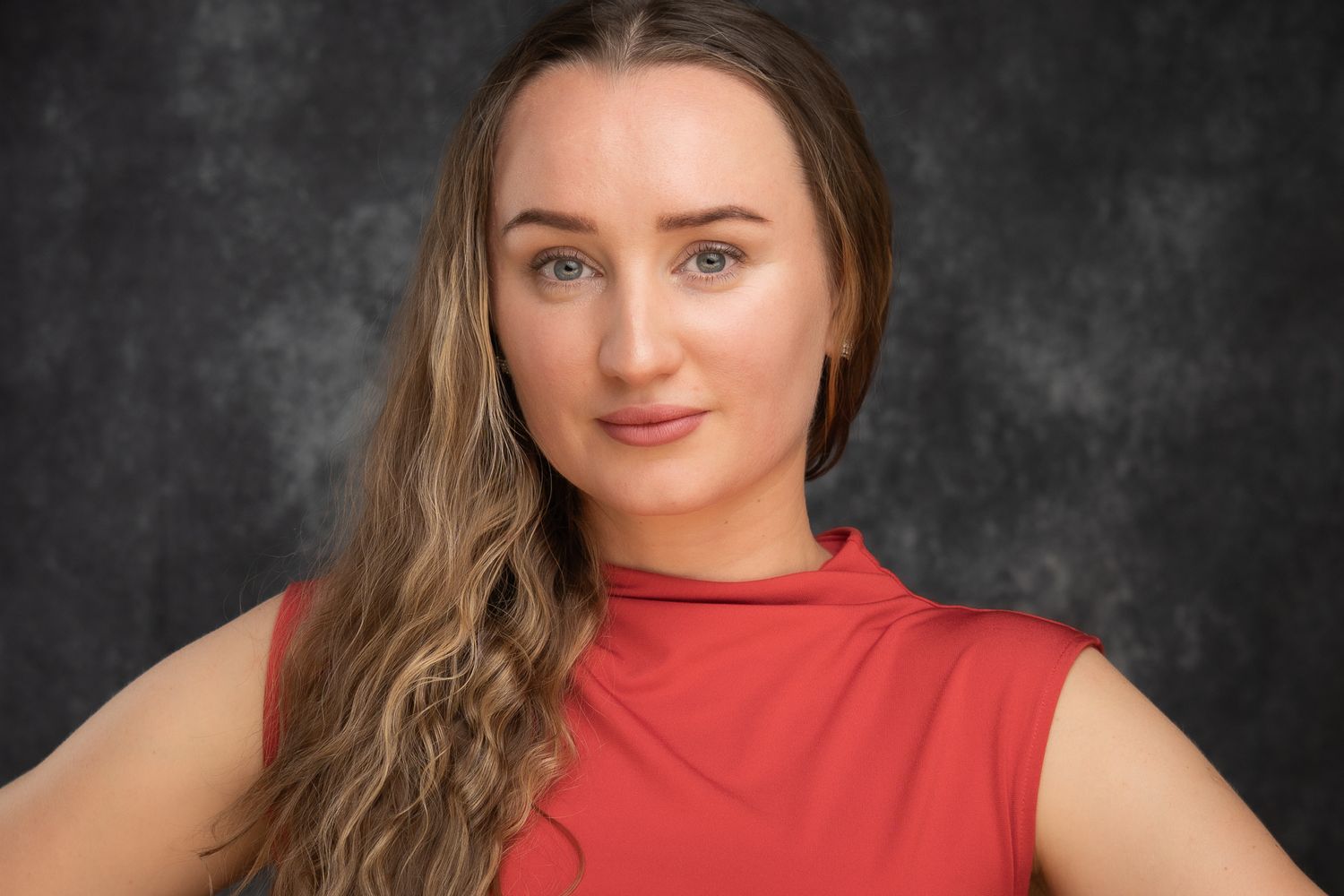 Studio headshot of a woman in a red top against a dark textured background.