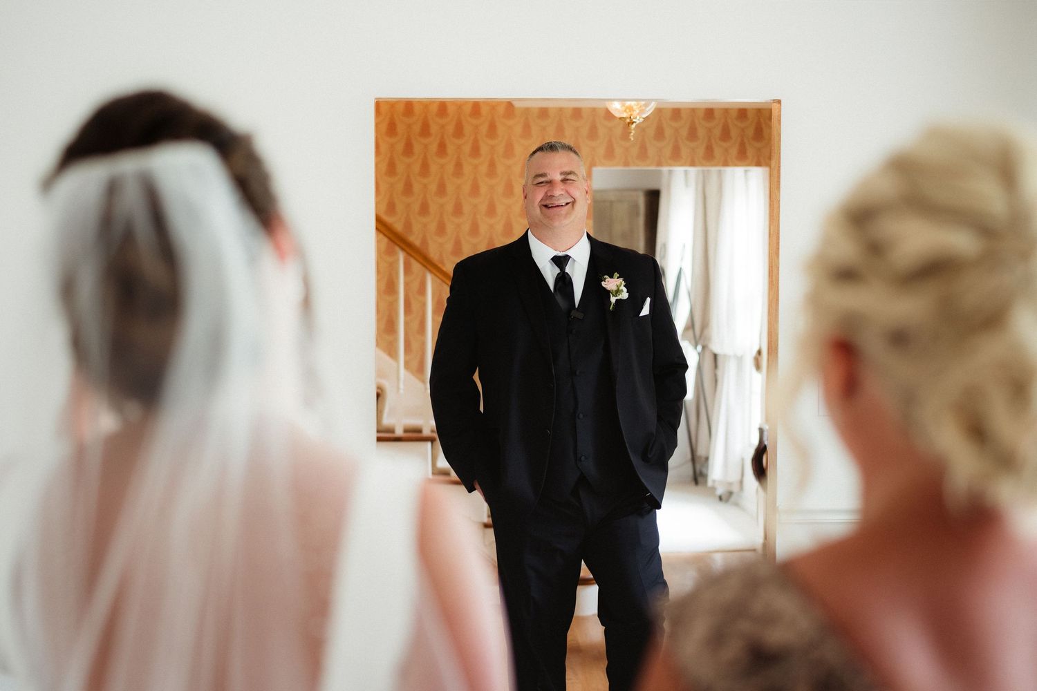 Groom in black suit smiling at bride during first look moment at elegant wedding venue.