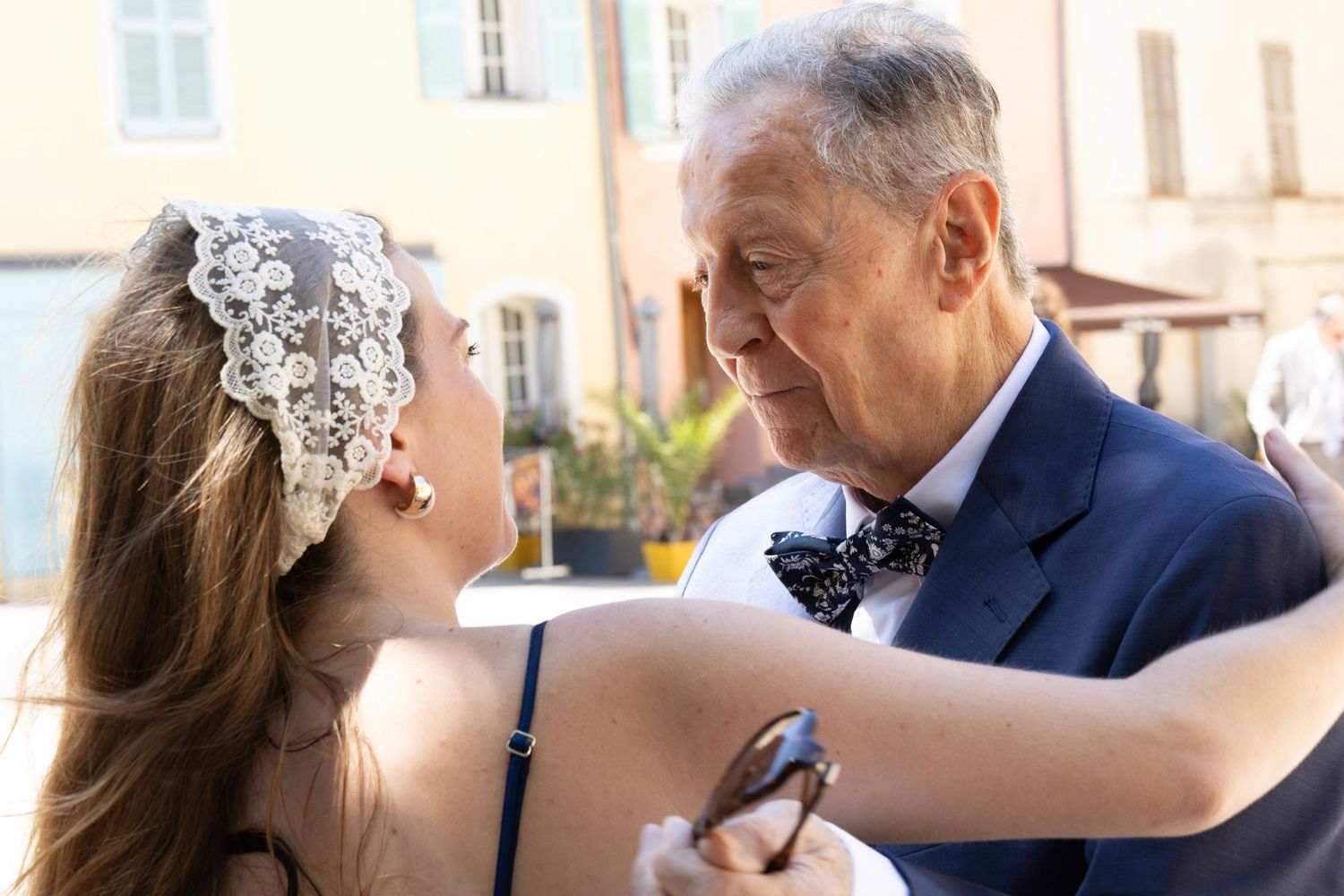 Une invitée ajuste le nœud papillon d’un homme en costume bleu.