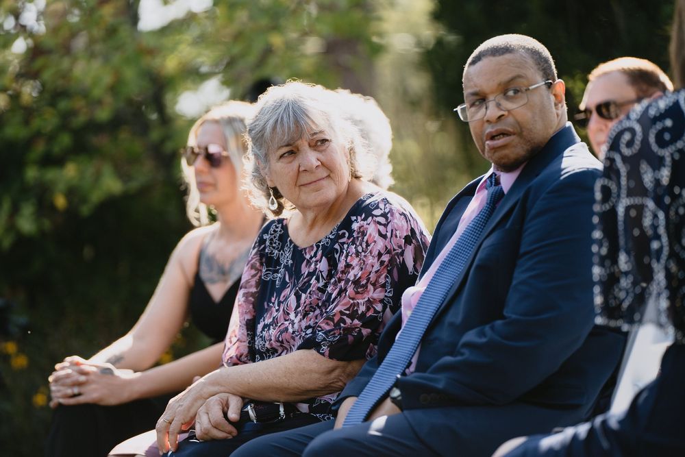 Diverse group of adults seated outdoors at a formal event, including an elderly woman and man in a suit.