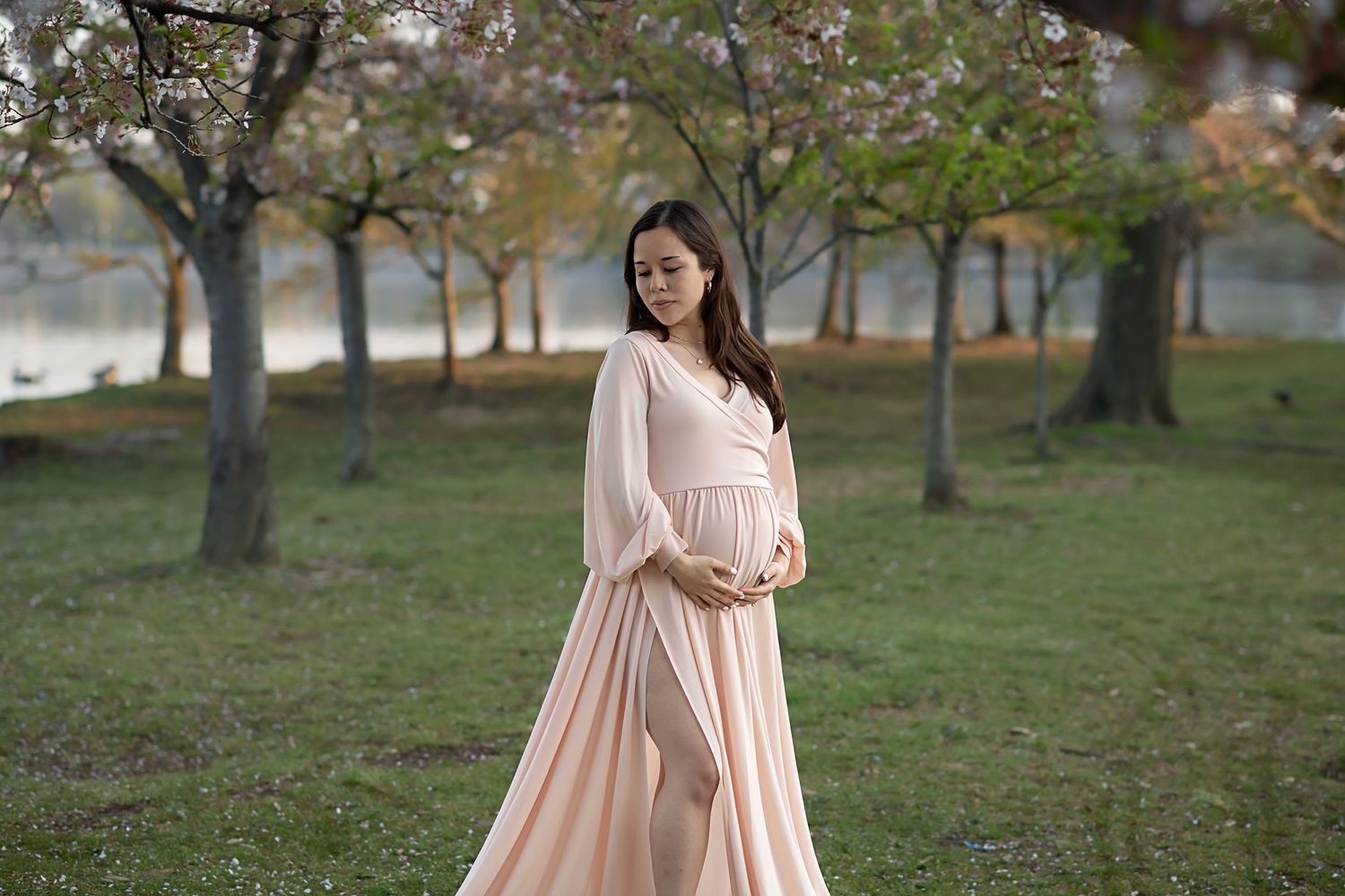 Woman in flowing pink dress poses elegantly among spring trees.