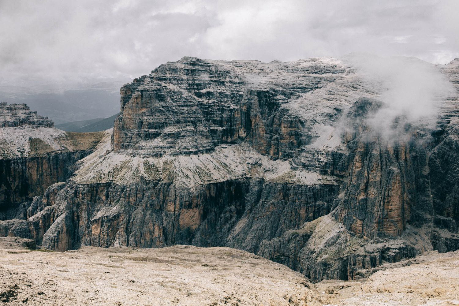 Dramatic Dolomite mountains with jagged rocky peaks, winding road, and moody overcast sky in the Italian Alps.