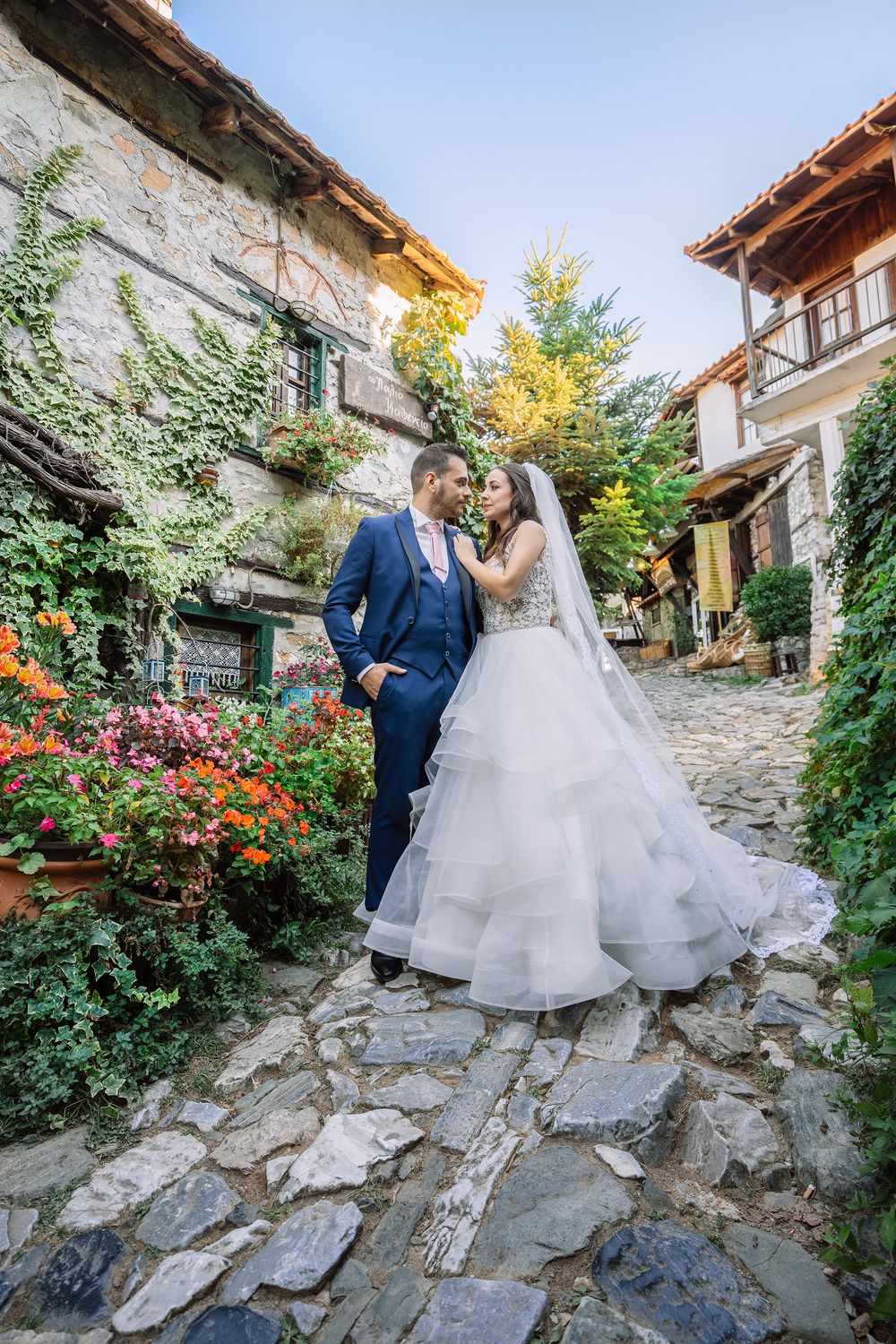 Wedding couple standing on a cobblestone street of a traditional Greek village with flowers.