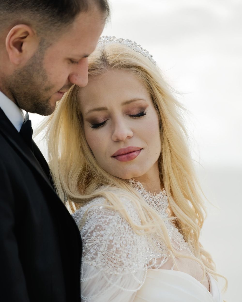 Close-up wedding portrait of groom looking at blonde bride with eyes closed.