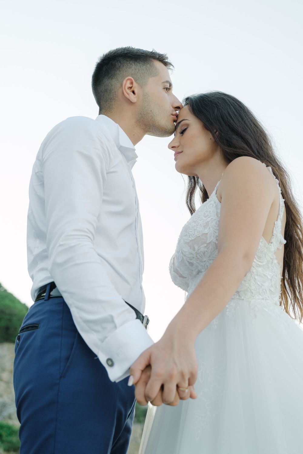Groom in a white shirt gently kissing his bride on the forehead.