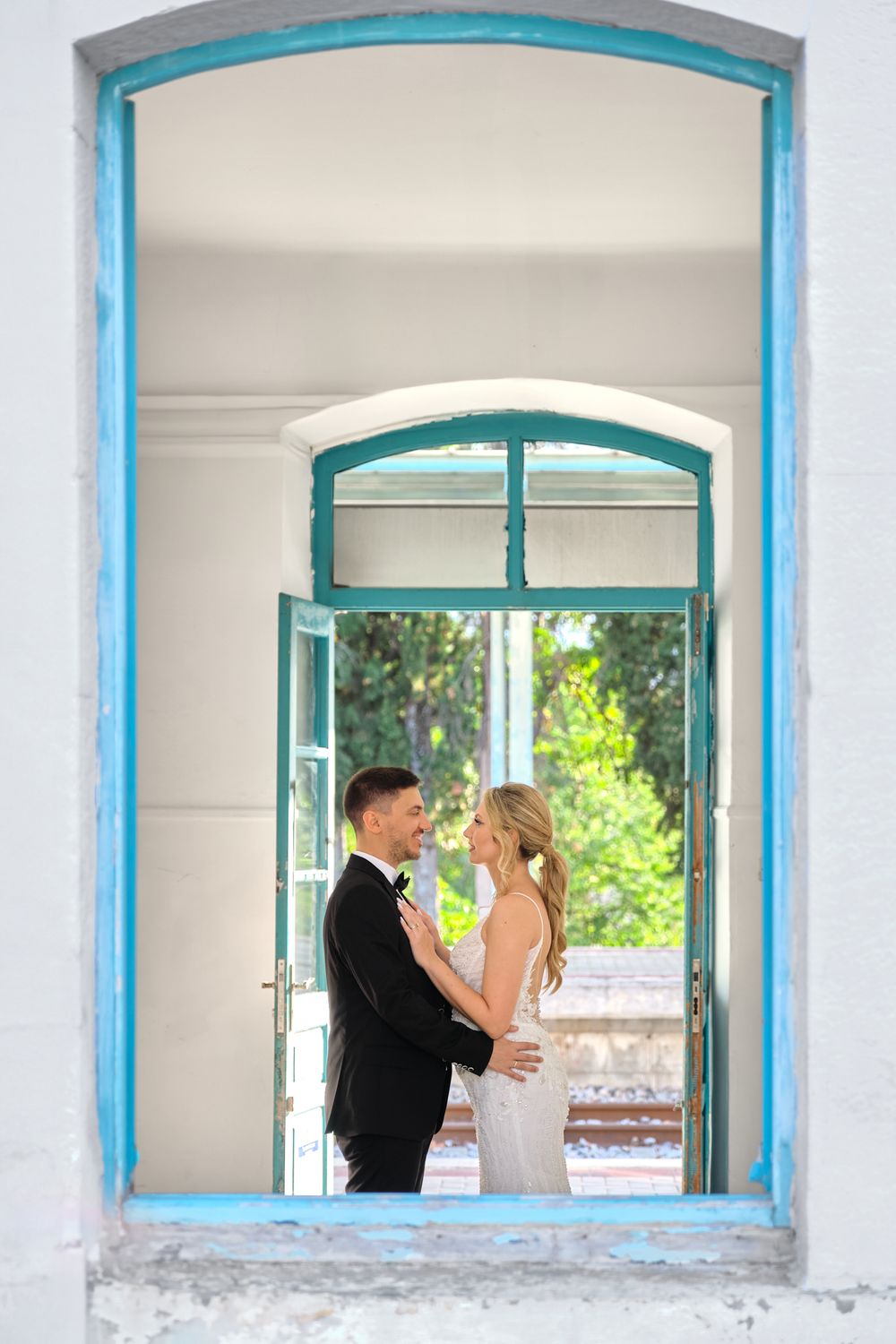 Wedding couple embracing inside a window frame with light blue shutters in Greece.
