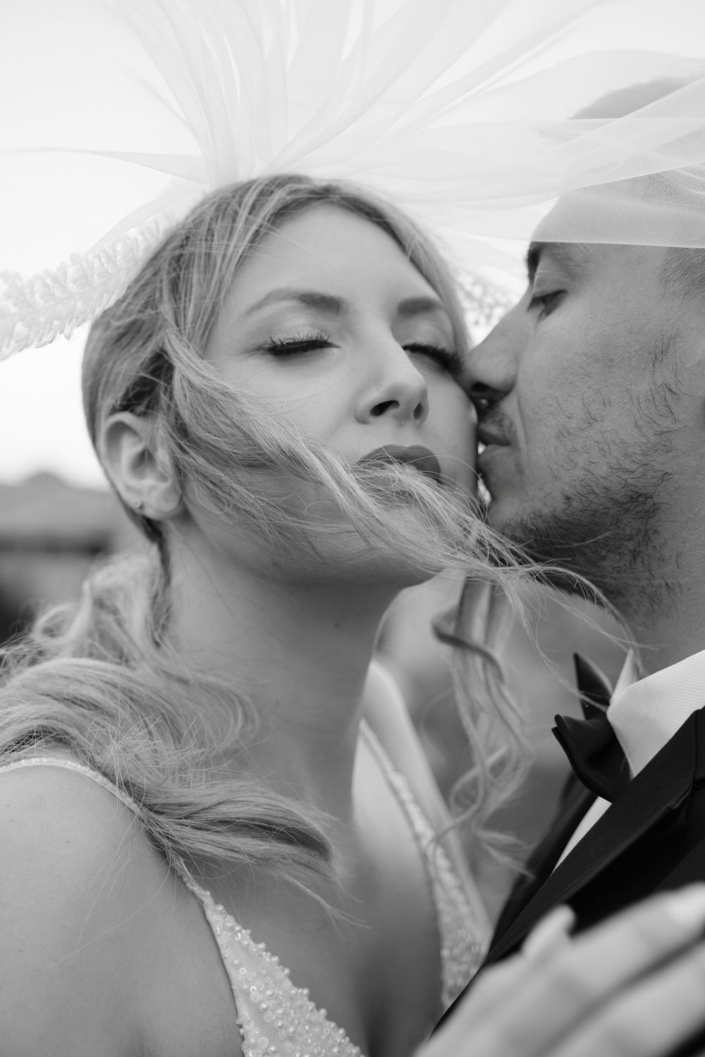Black and white close-up portrait of a groom kissing the bride on her cheek.