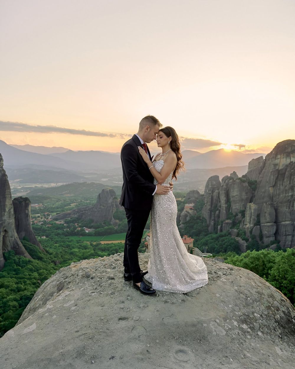 Wedding couple embracing on a high cliff with the Meteora rock formations at sunset.
