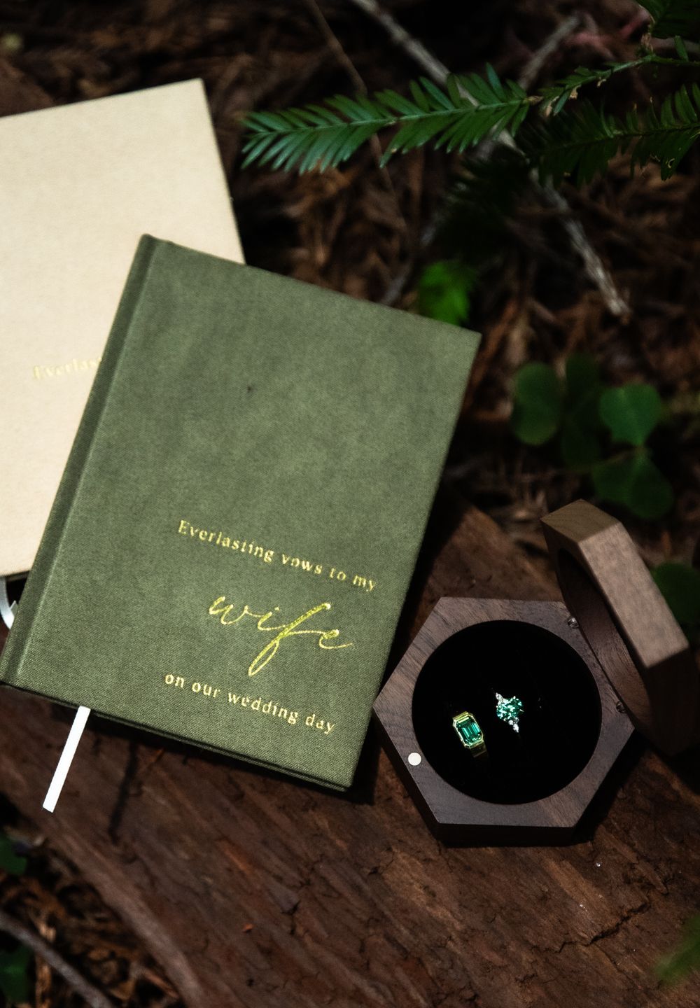 emerald wedding bands and lesbian couple's velvet vow books on the forest floor