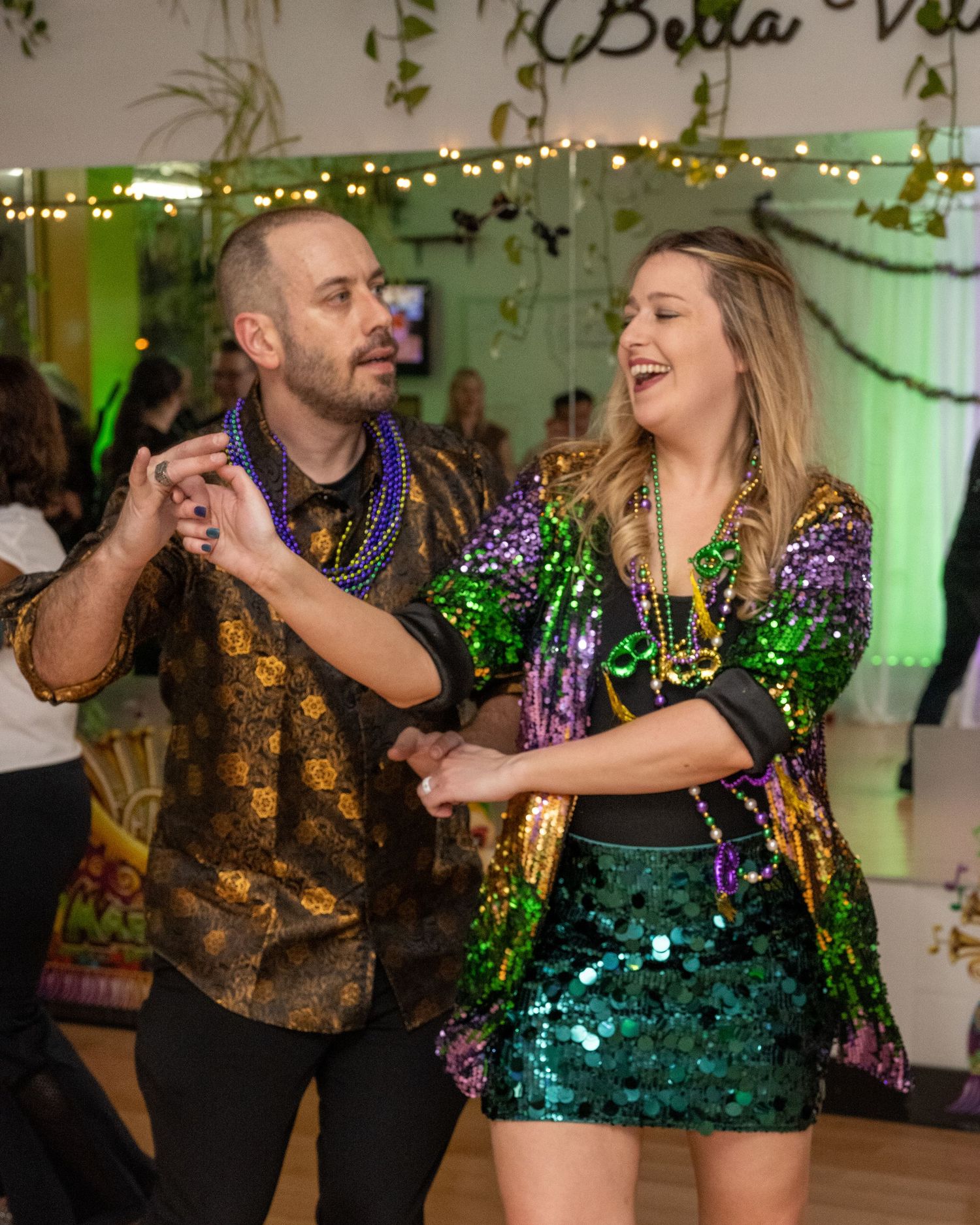 Couple dancing in Mardi Gras outfits with colorful beads and sequins at a festive latin dance social