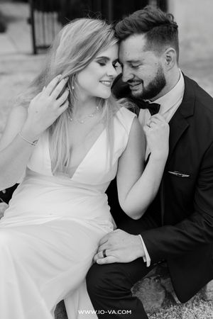 Black and white wedding photo of a smiling bride in white gown and groom in tuxedo sitting closely together.