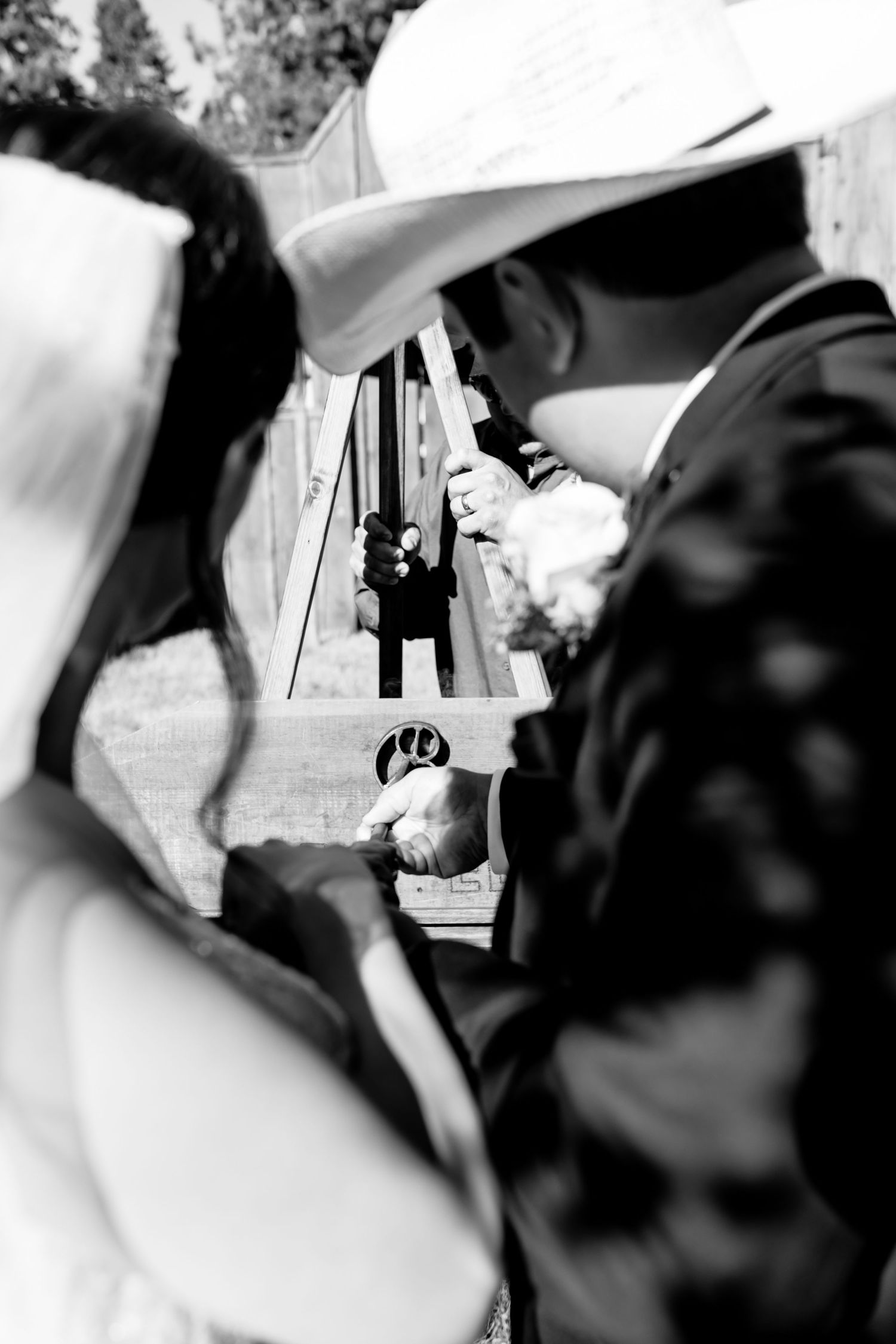 Black and white wedding photo of bride and groom holding hands, with photographer captured in background reflection.