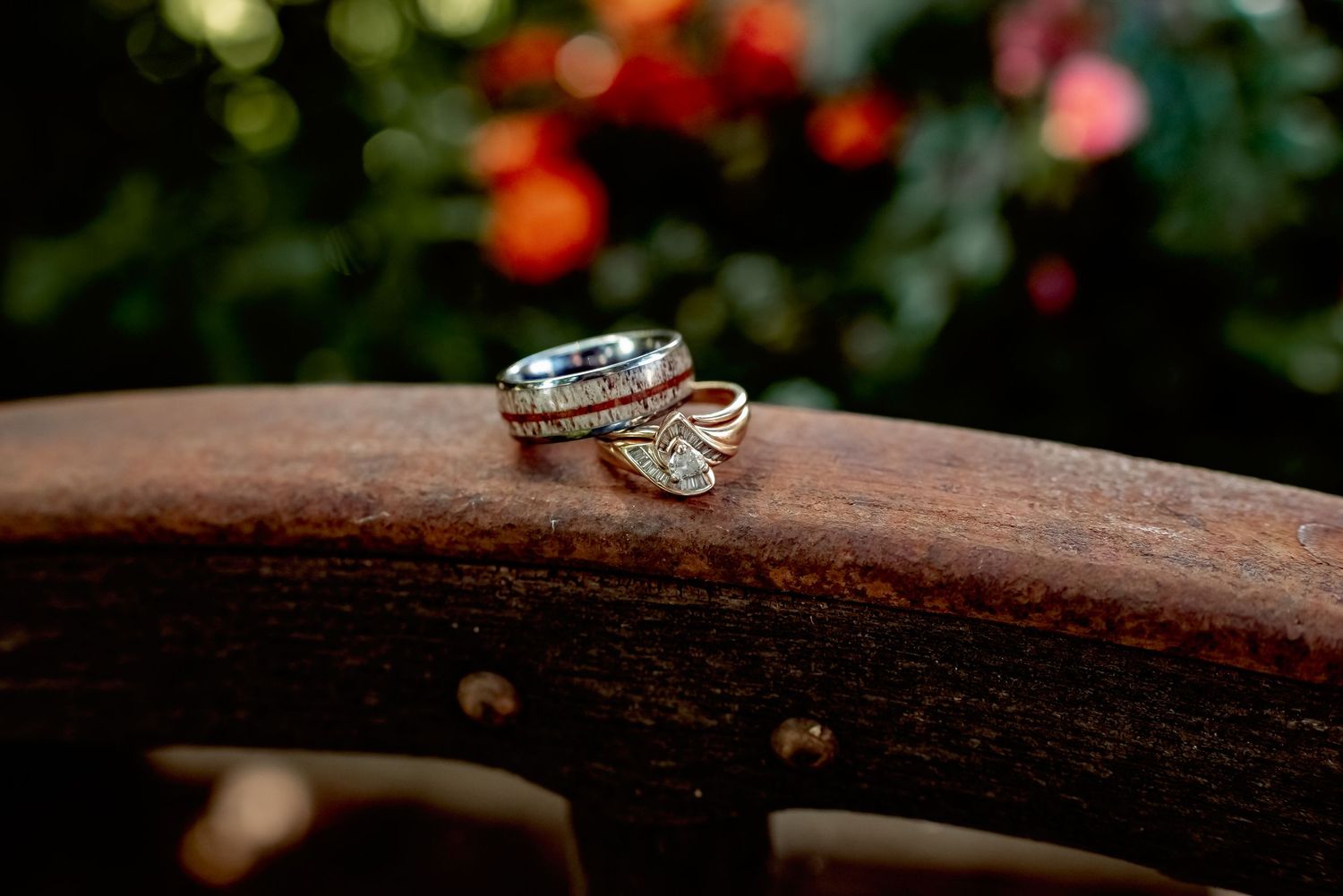 Close-up of elegant wedding rings stacked on a rustic wooden surface with bokeh floral background.