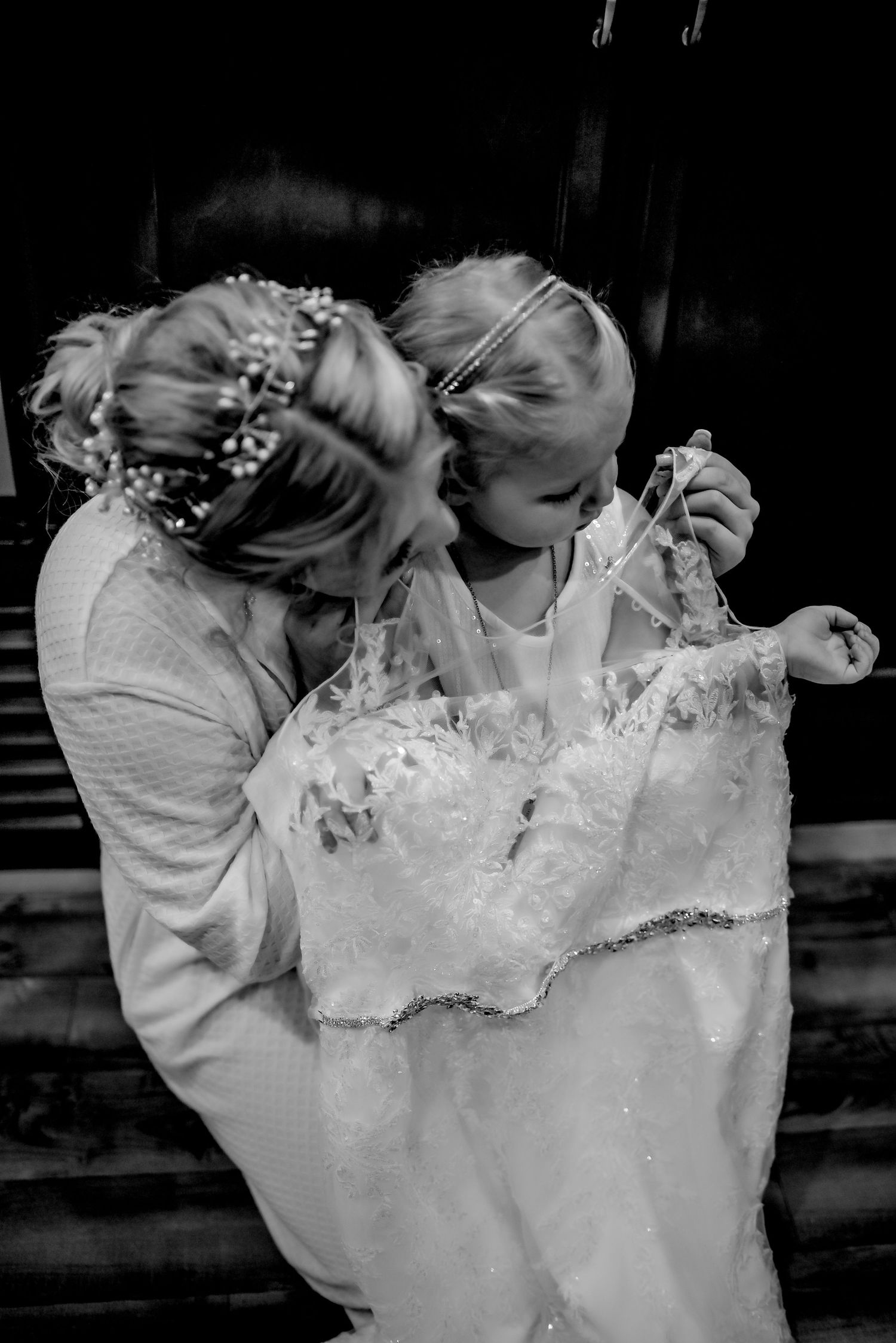 Black and white photo of a bride holding a young flower girl in a white dress at a wedding ceremony.