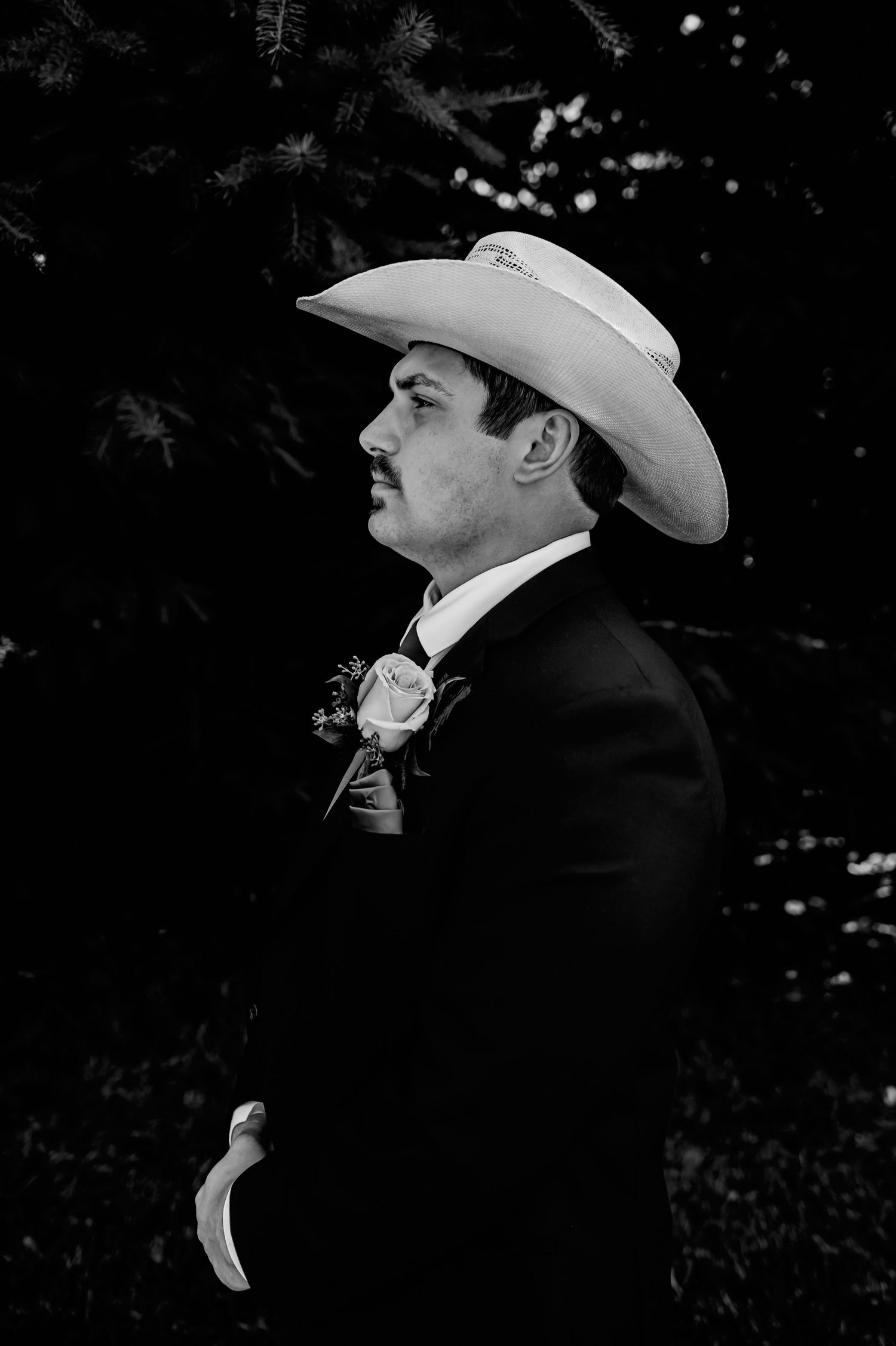 Black and white portrait of a groom in a cowboy hat and suit with boutonniere at a western wedding.
