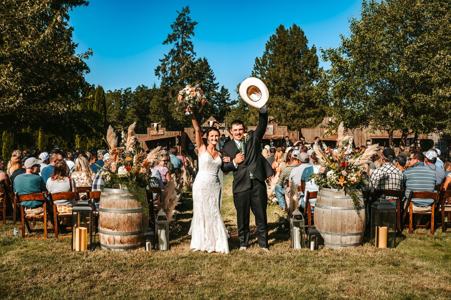 Bride and groom celebrate outdoors at rustic winery wedding ceremony with barrel decor and guests seated on wooden chairs.