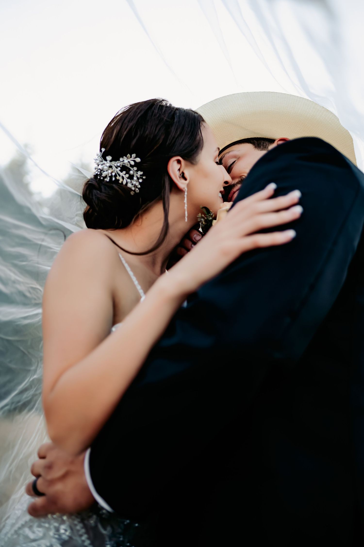 Bride and groom sharing an intimate kiss under a flowing veil at their wedding.