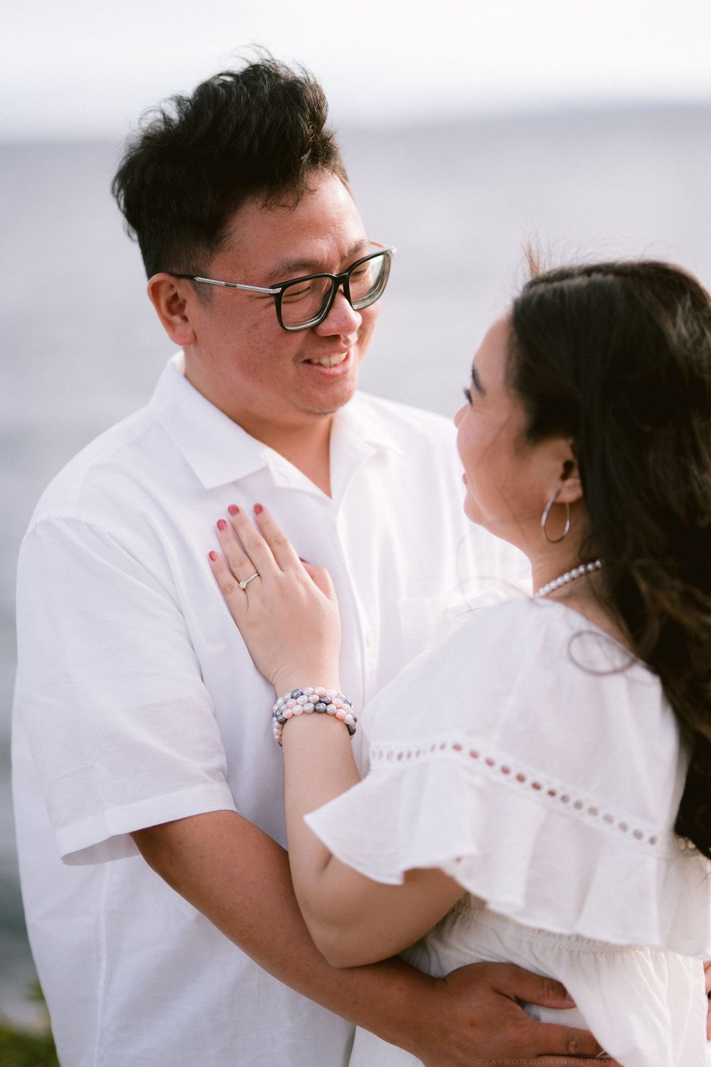 Close-up of Asian couple in white outfits sharing a tender moment, woman wearing pearl necklace and bracelet.