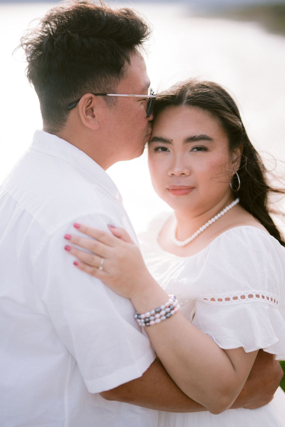 Asian couple in white sharing intimate moment outdoors in bright sunlight.