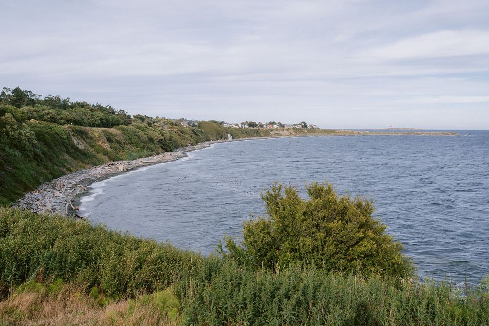 Scenic coastal bay with green cliffs, calm blue waters, and a small seaside village under a cloudy sky.