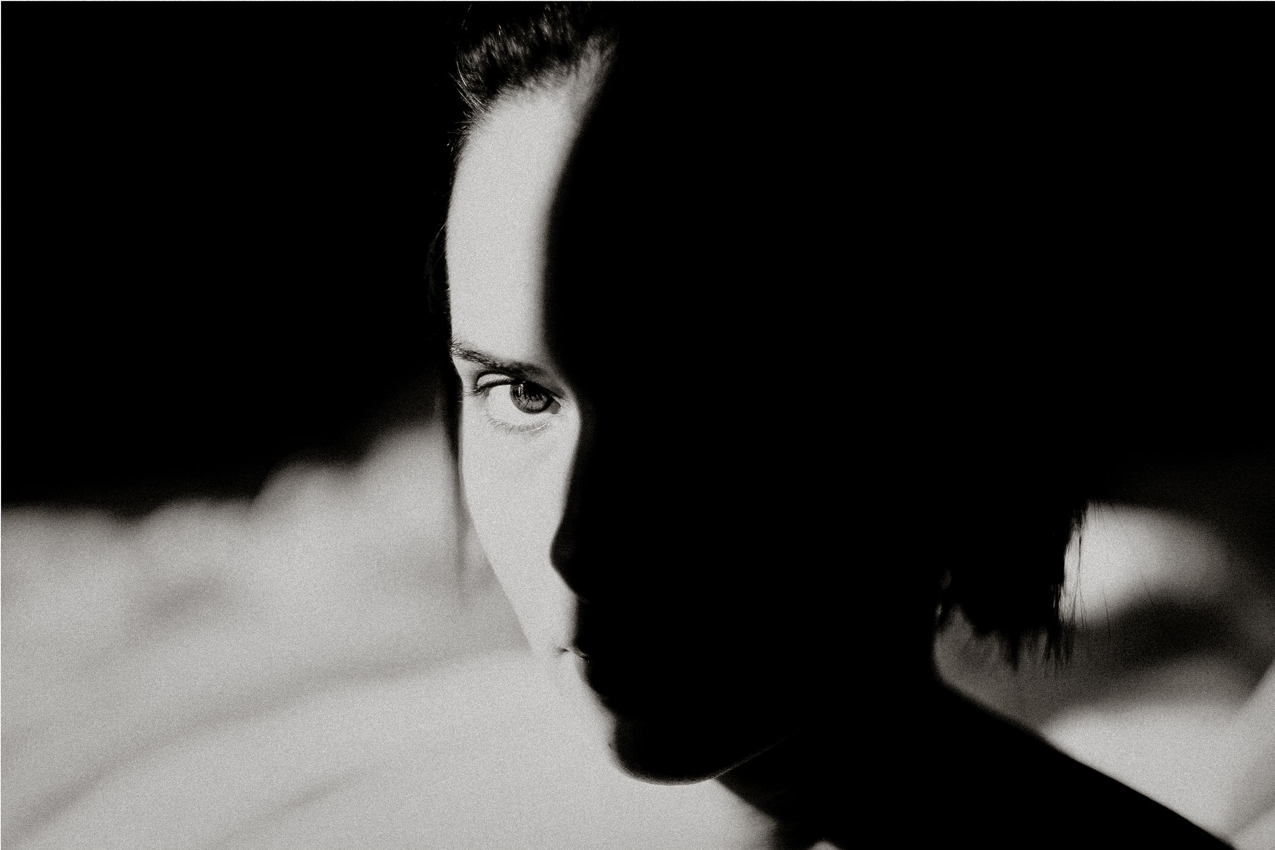 Black and white portrait of a person with half their face illuminated, creating a dramatic shadow effect.