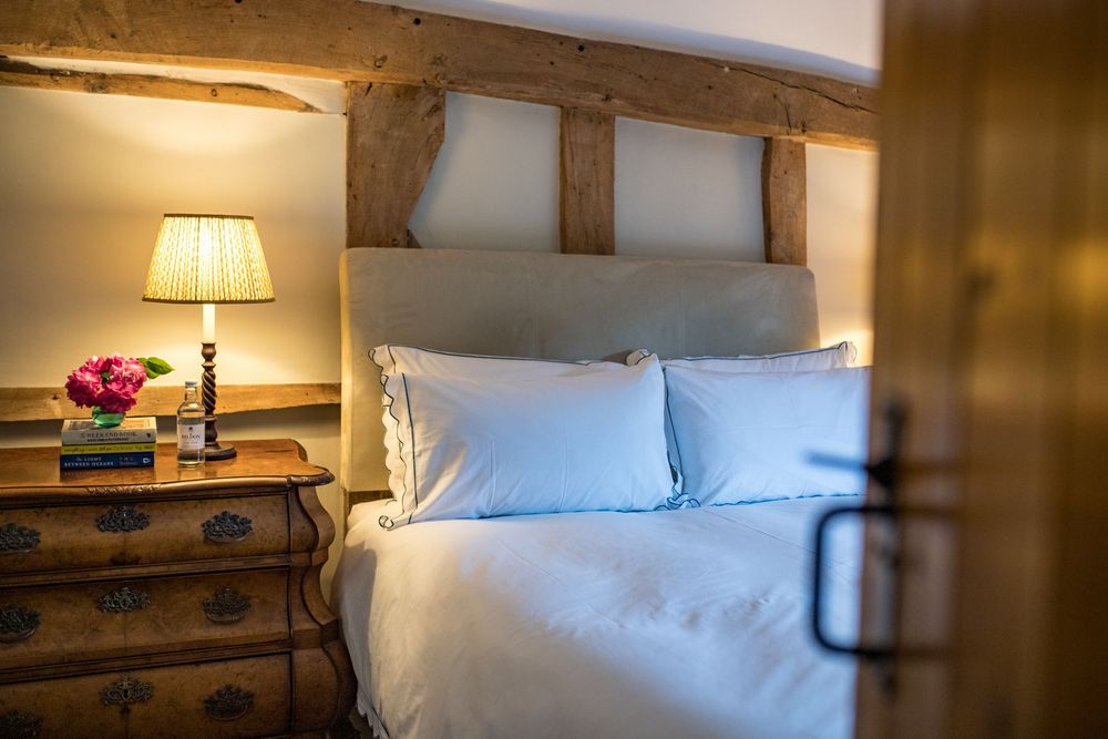 Cozy bedroom interior with rustic wooden beams, blue pillows, and vintage nightstand with warm lamp lighting.