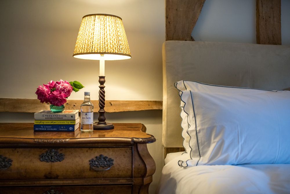 Bedside wooden nightstand with traditional table lamp and pink flowers in a cozy bedroom setting.