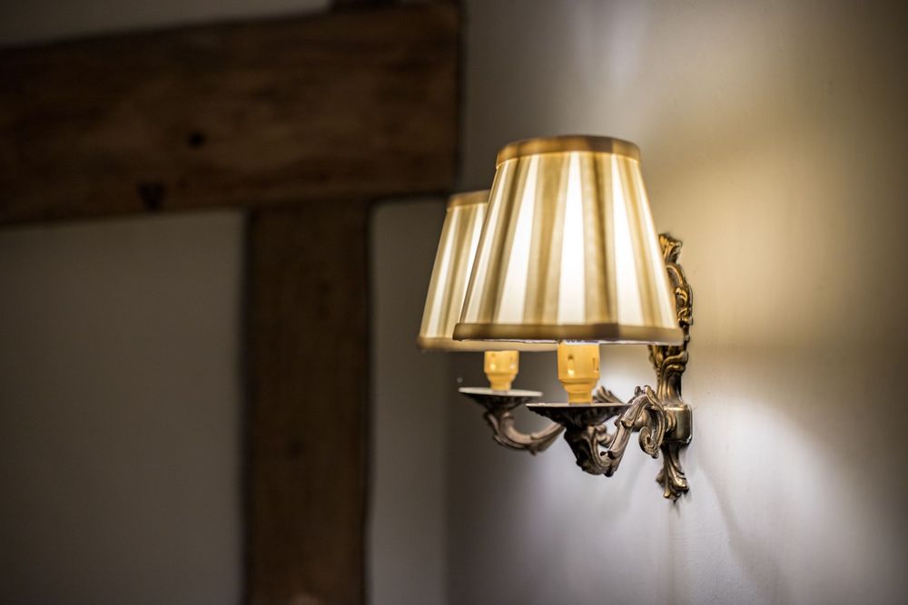 An elegant antique wall sconce with a pleated fabric lampshade casts warm light against a rustic wooden beam wall.