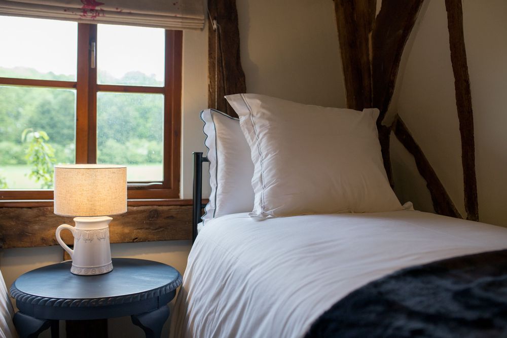A cozy attic bedroom with exposed wooden beams, white bedding, and a bedside table with a coffee mug and lamp.
