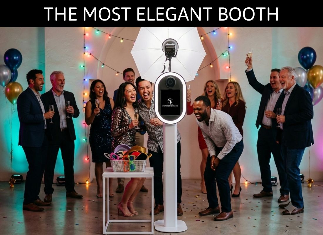 Elegant photo booth stand surrounded by lush floral arrangements of pink and white roses at a wedding venue.