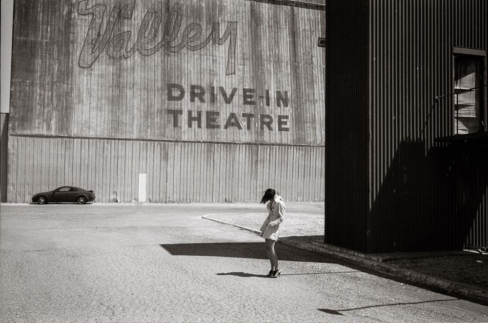 Black and white photo of a child holding a stick outside a Valley Drive-In Theatre building.