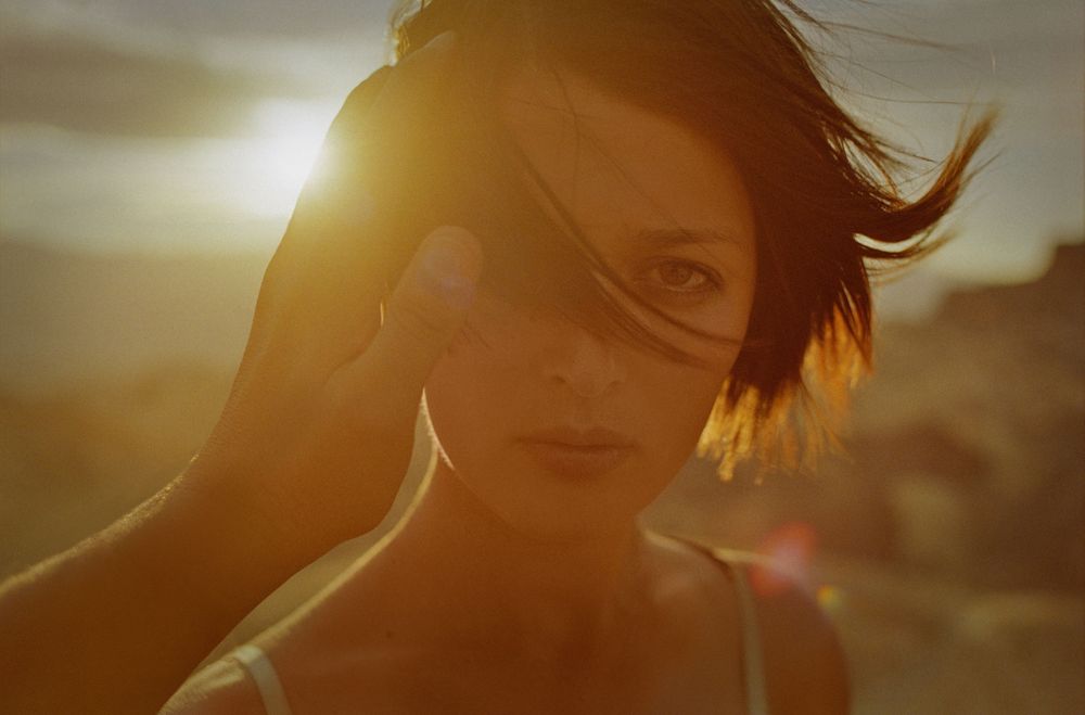 Golden sunset portrait of a young woman with short dark hair, warm light illuminating her face in a desert setting.