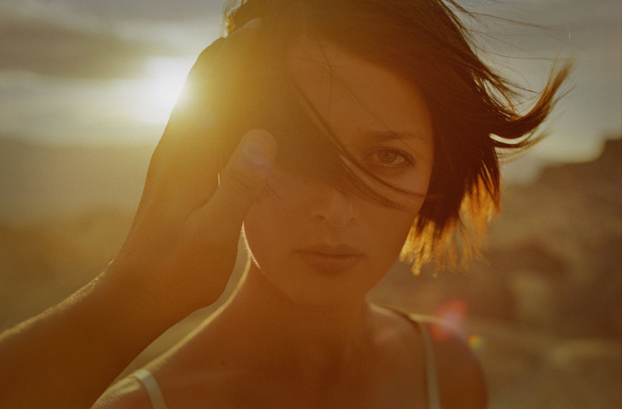 Golden sunset portrait of a young woman with short dark hair, warm light illuminating her face in a desert setting.