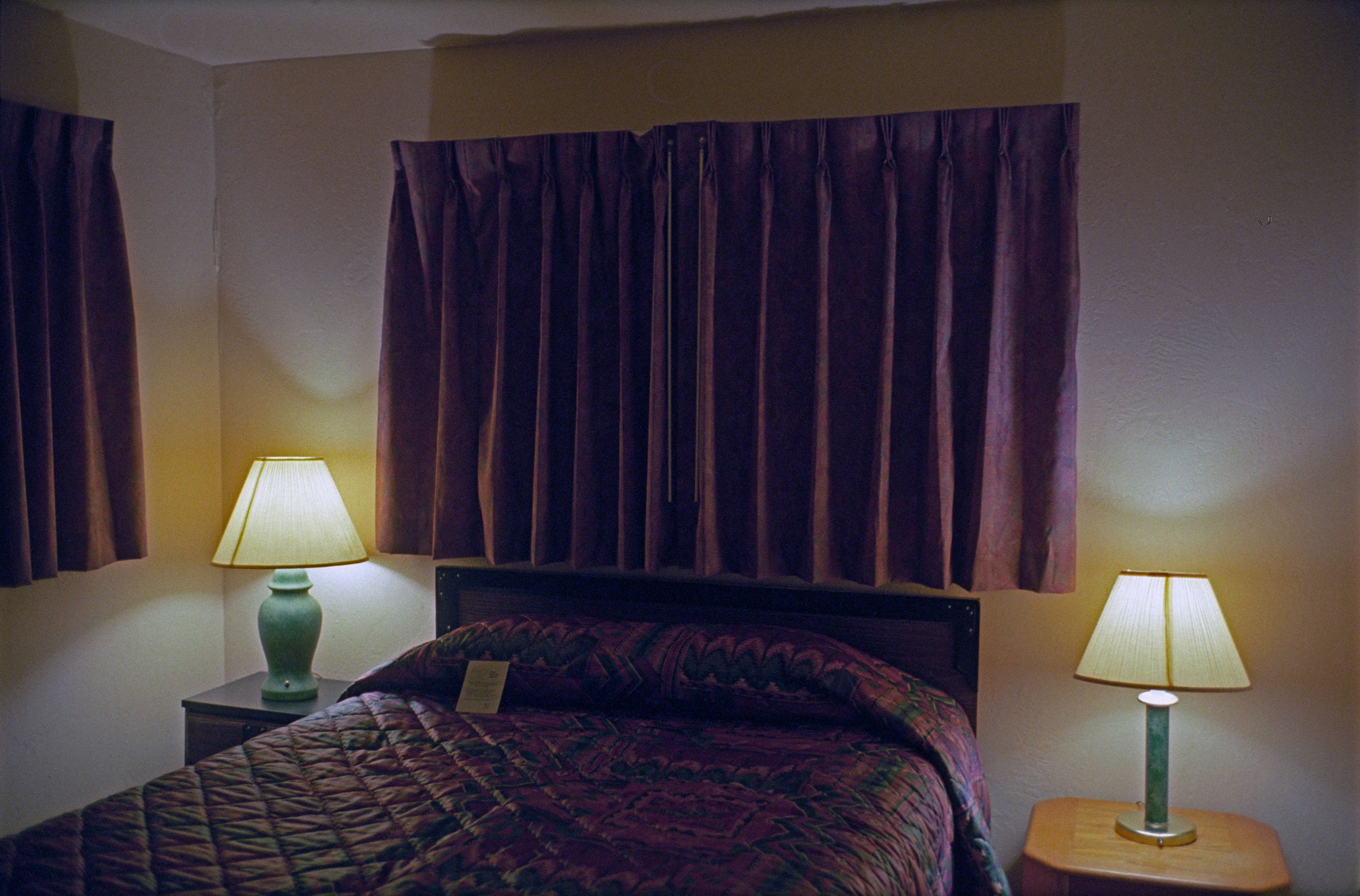 Cozy motel room with a queen bed, two lamps, and dark curtains.