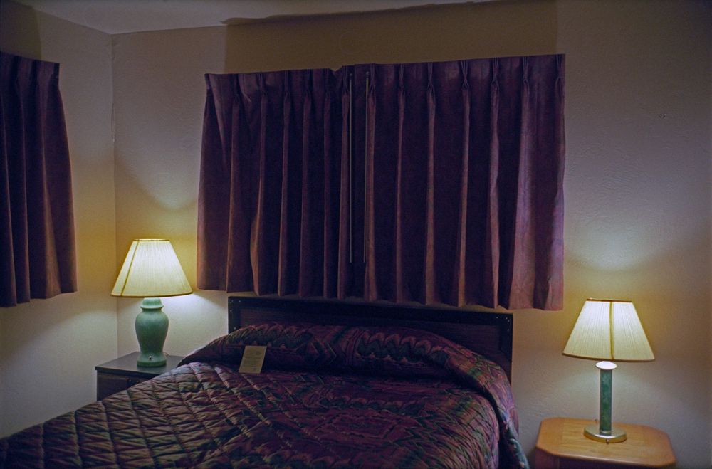 Cozy motel room with a queen bed, two lamps, and dark curtains.