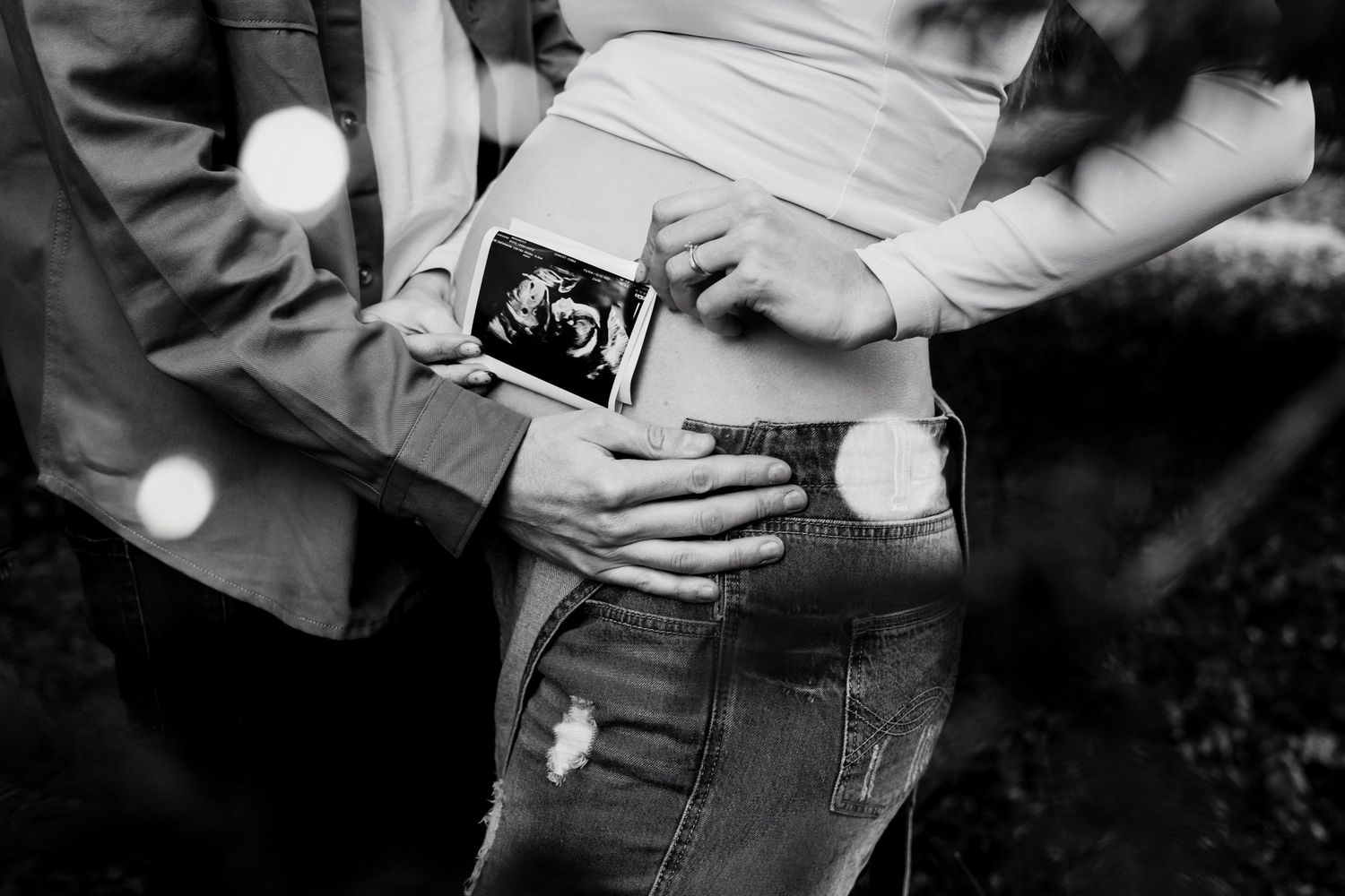 Black and white close-up of expectant parents holding an ultrasound scan against a pregnant belly.