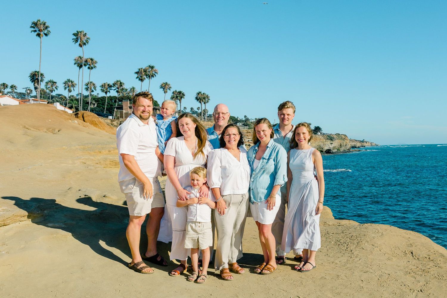 San Diego family portrait photography of a large multi-generational group posing at Sunset Cliffs with palm trees and ocean waves.