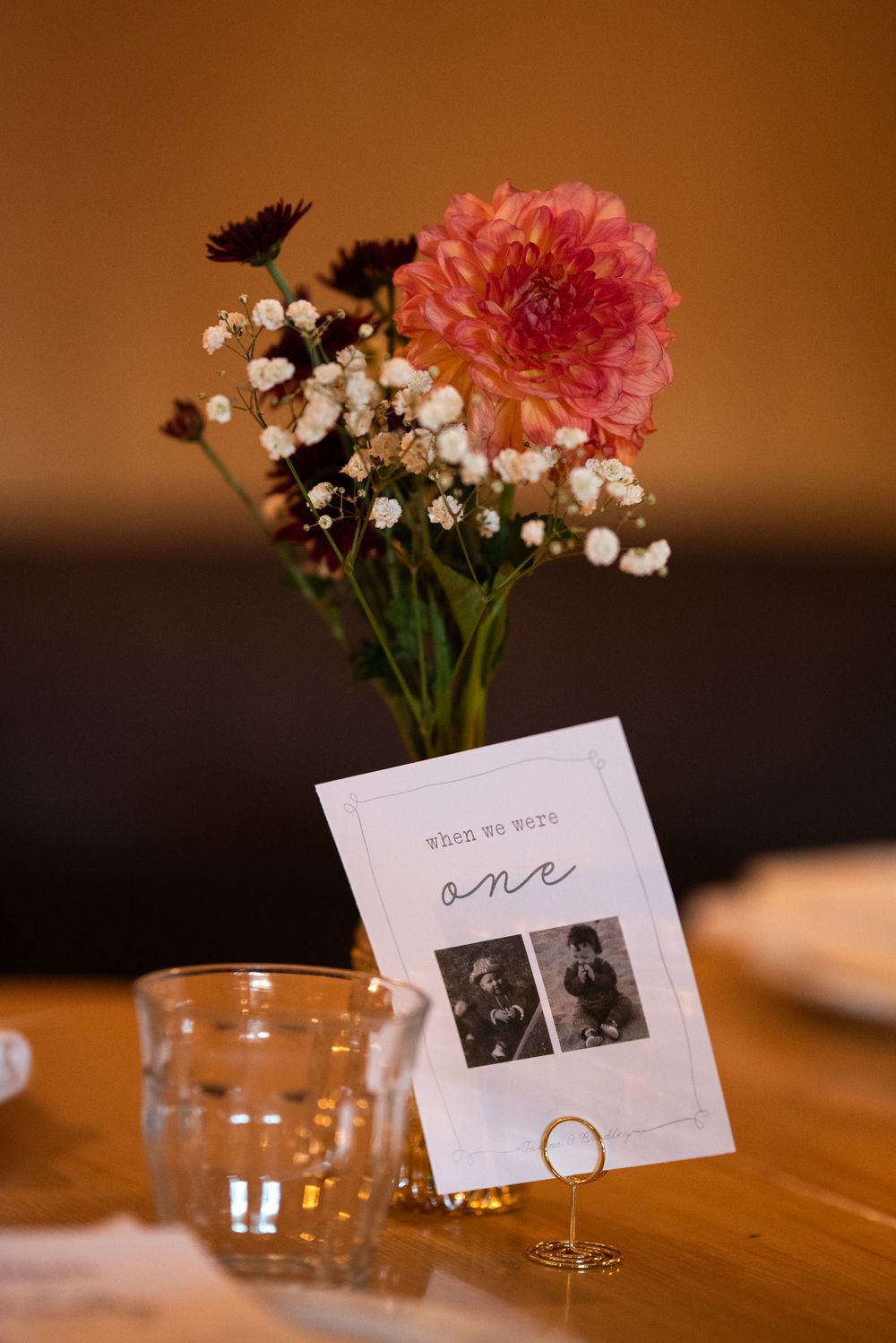 Wedding table centerpiece with pink dahlia, baby's breath, table number card reading 'one', and glass vase.