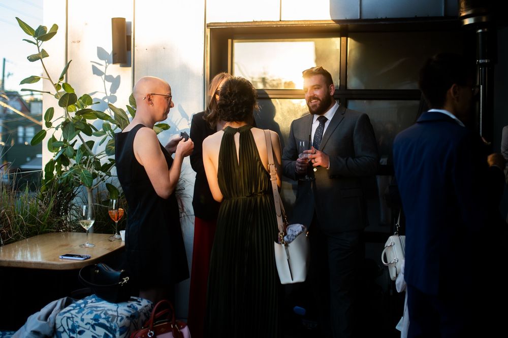 Elegantly dressed guests mingle at an upscale rooftop cocktail party during golden hour.