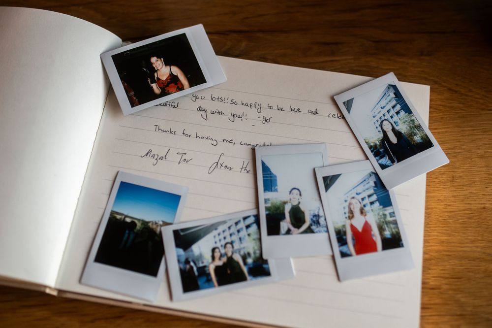 Open guest book with handwritten notes and scattered Polaroid photos on a wooden table.