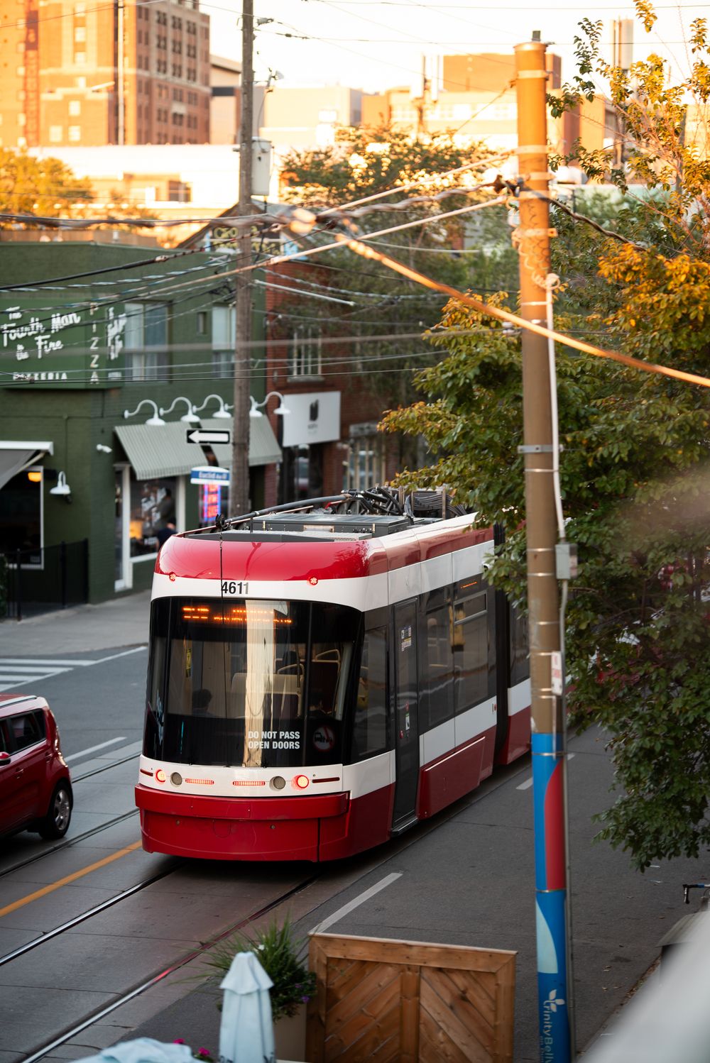 Red and white TTC streetcar traveling along urban tracks in Toronto at golden hour with city buildings in background.