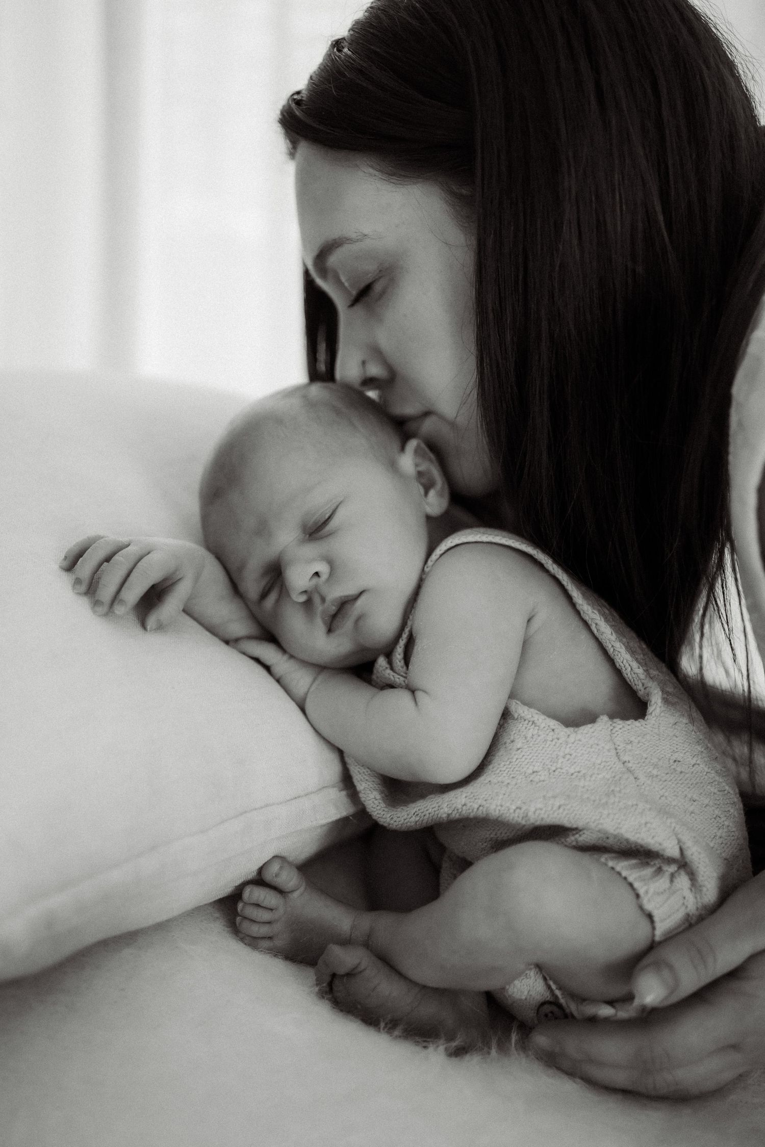 Black and white photo of a mother tenderly kissing her sleeping newborn baby resting on a white pillow in Buxton, Victoria