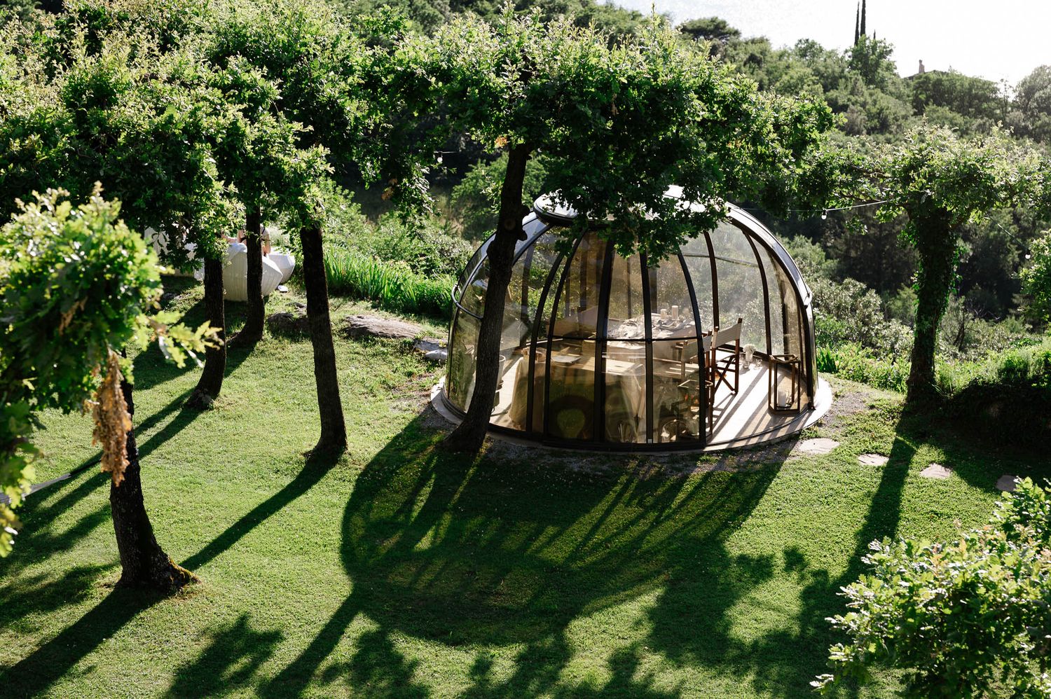 Unique glass dome dining structure surrounded by lush green garden and olive trees.