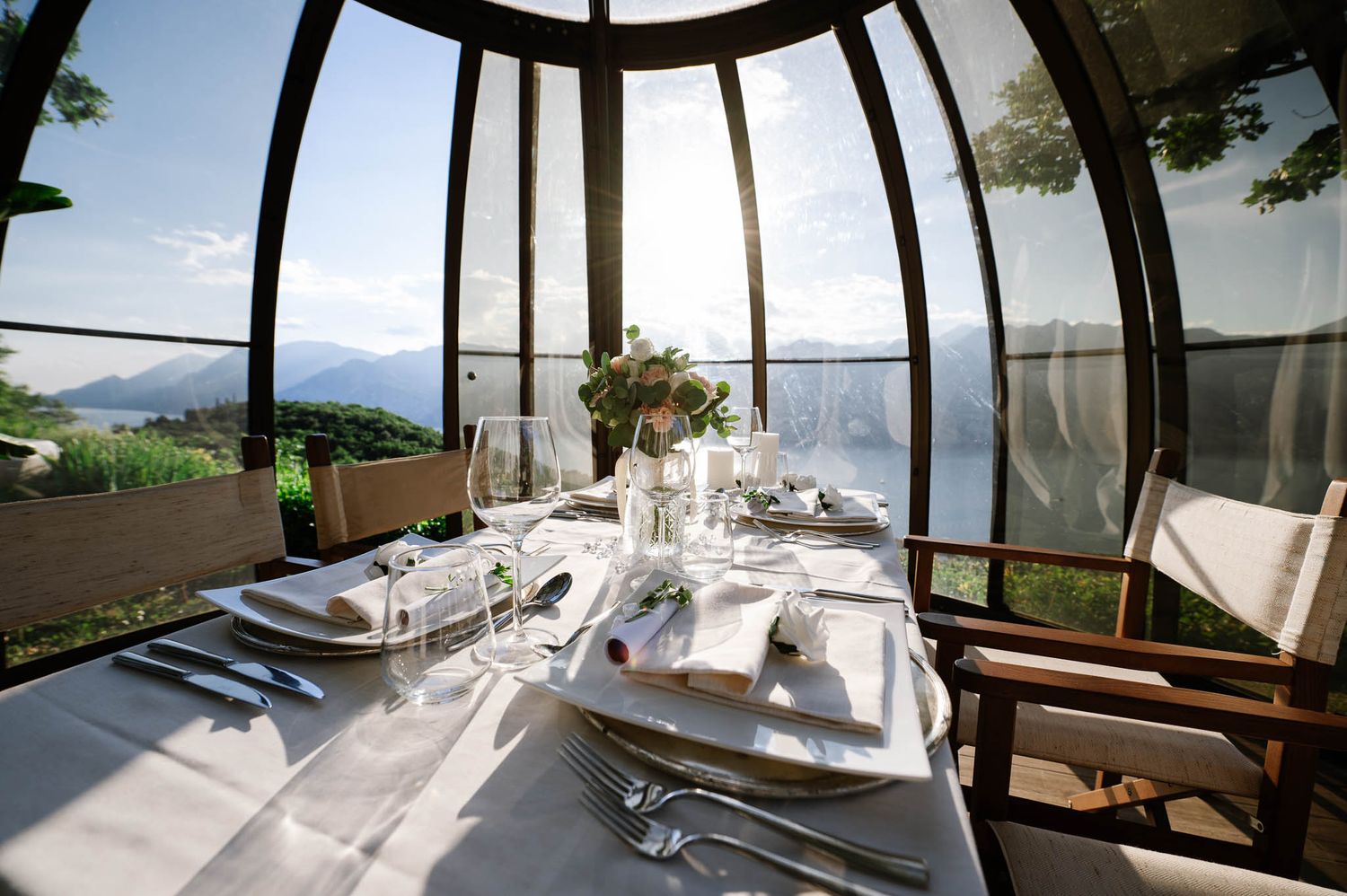Romantic lakeside restaurant dining table set for a wedding reception in a glass-enclosed pavilion with panoramic views.