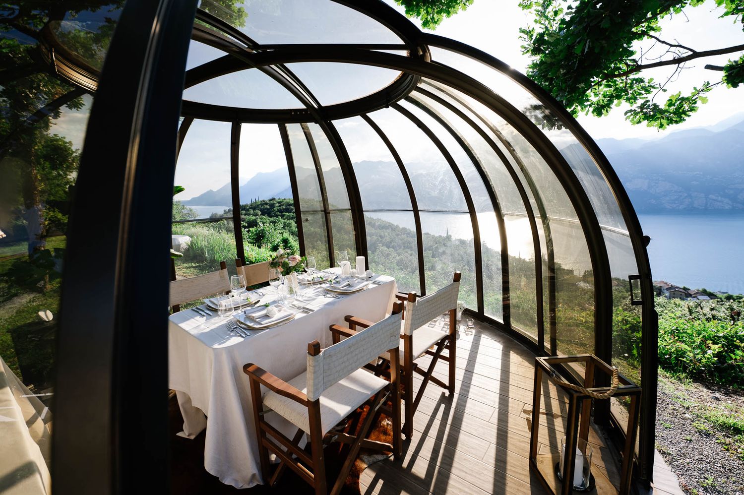 Elegant glass greenhouse dining space with white tablecloth and stunning panoramic lake and mountain views.