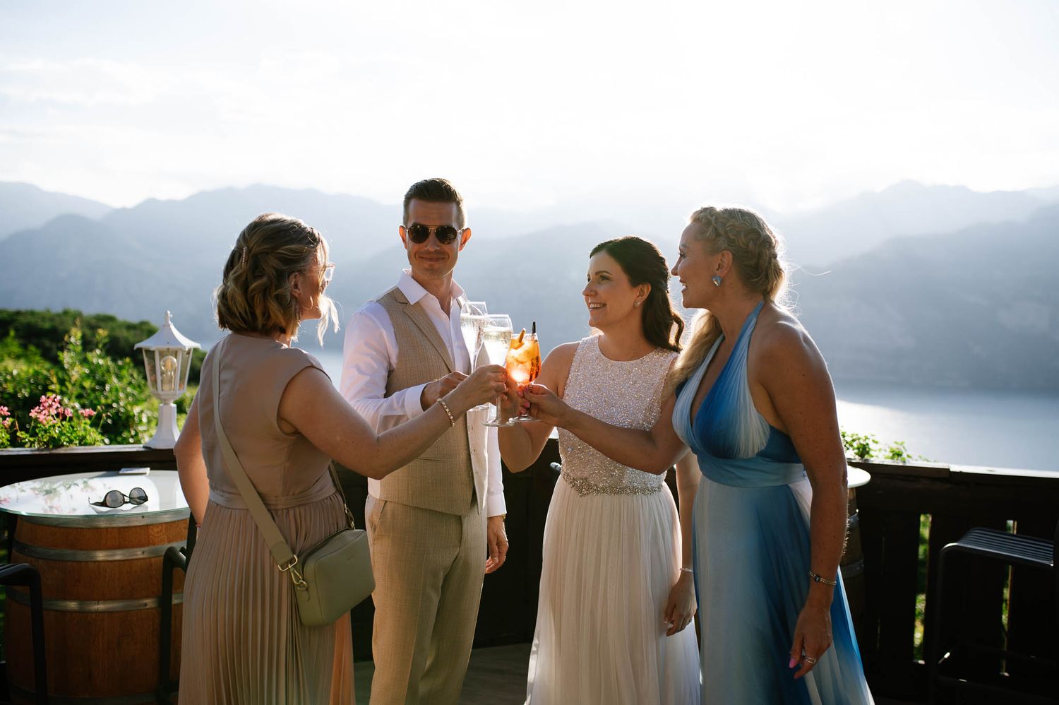 Wedding party toasting with champagne on a scenic mountain terrace overlooking a stunning lake view.