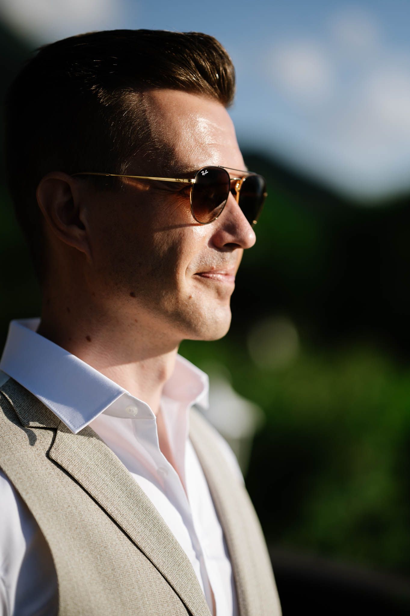 Close-up portrait of a stylish groom wearing aviator sunglasses and linen vest on wedding day.