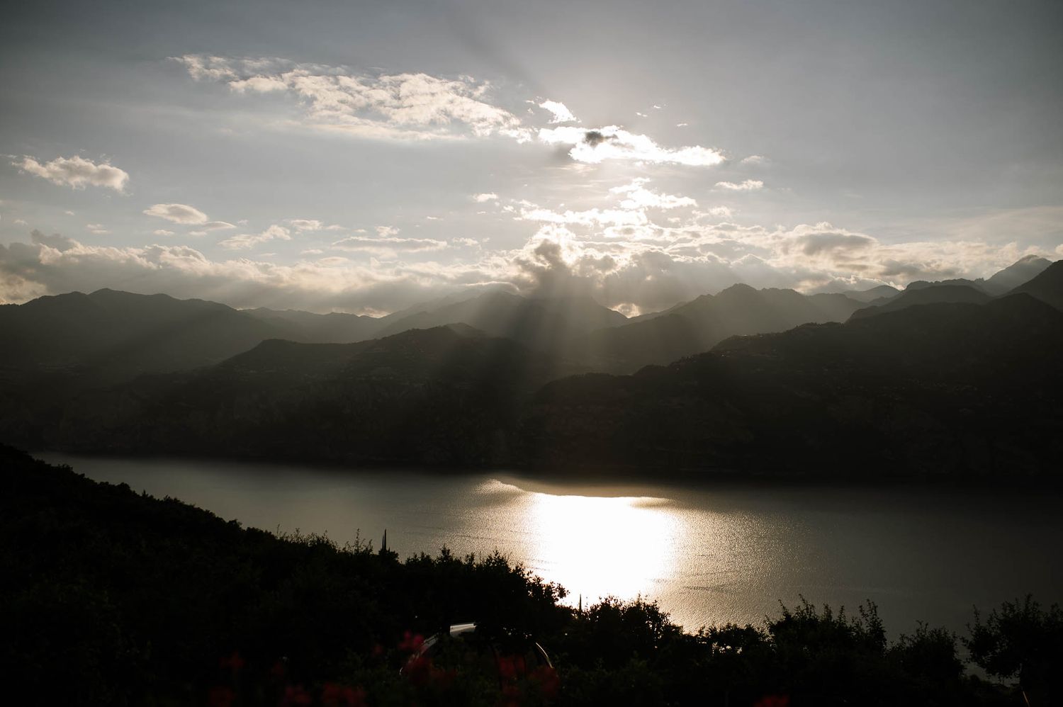 Dramatic sunset over a mountain lake with sun rays breaking through clouds over silhouetted hills.